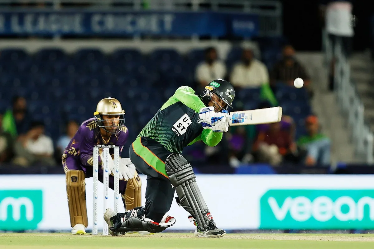 A batter playing a shot as the wicketkeeper looks on
